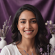 Smiling South Asian woman in her late 20s, looking happy and content against a deep violet background.